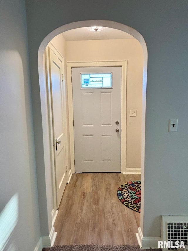 doorway with arched walkways, visible vents, baseboards, and light wood-style floors