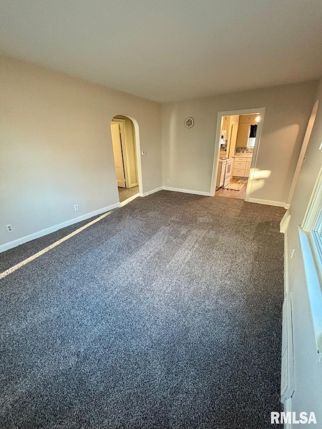 empty room with dark colored carpet, baseboards, and arched walkways