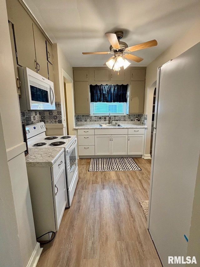 kitchen featuring white appliances, light wood-style flooring, tasteful backsplash, and a sink