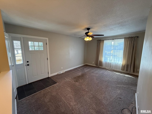 entrance foyer featuring visible vents, baseboards, a textured ceiling, a ceiling fan, and dark colored carpet