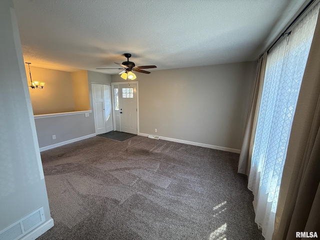 unfurnished room with visible vents, ceiling fan with notable chandelier, a textured ceiling, dark carpet, and baseboards