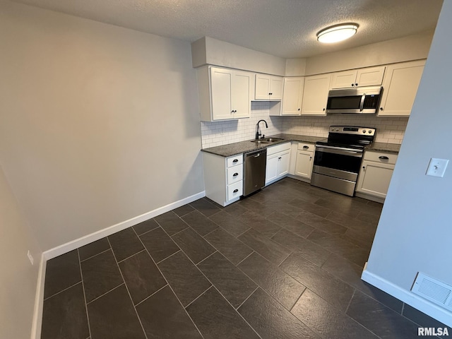 kitchen featuring dark countertops, decorative backsplash, appliances with stainless steel finishes, white cabinetry, and a sink