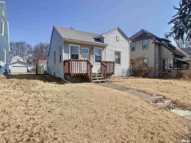 rear view of house featuring a deck, a detached garage, a lawn, and a shingled roof