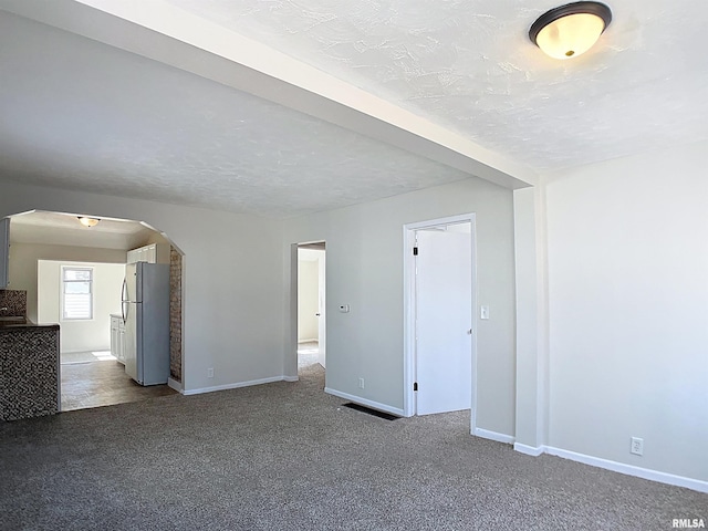 empty room featuring carpet flooring, baseboards, arched walkways, and a textured ceiling