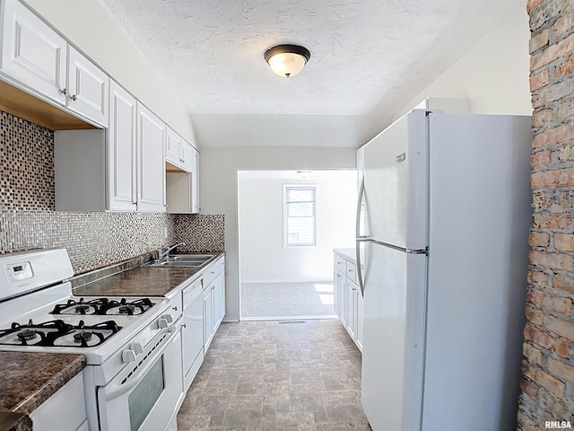 kitchen with white appliances, a sink, white cabinets, dark countertops, and tasteful backsplash