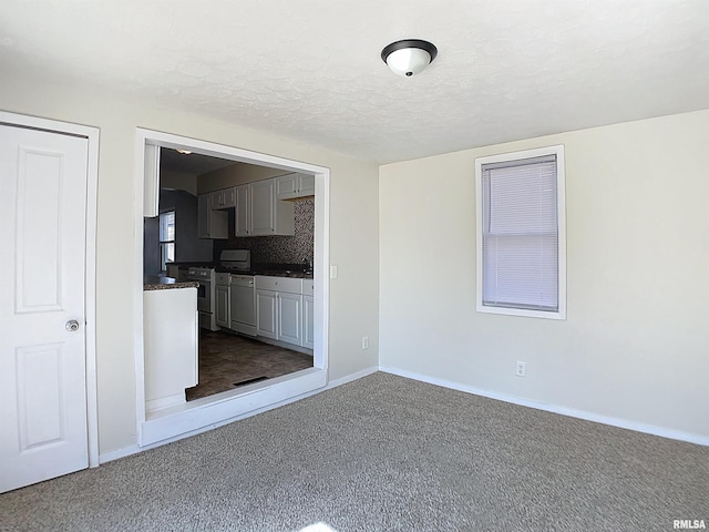 unfurnished living room with baseboards, dark carpet, and a textured ceiling