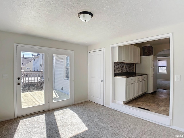 kitchen featuring a textured ceiling, decorative backsplash, freestanding refrigerator, and carpet floors