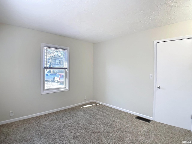 empty room with carpet flooring, baseboards, visible vents, and a textured ceiling