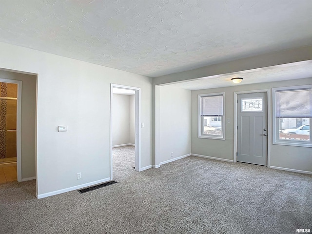 carpeted foyer with visible vents, baseboards, and a textured ceiling