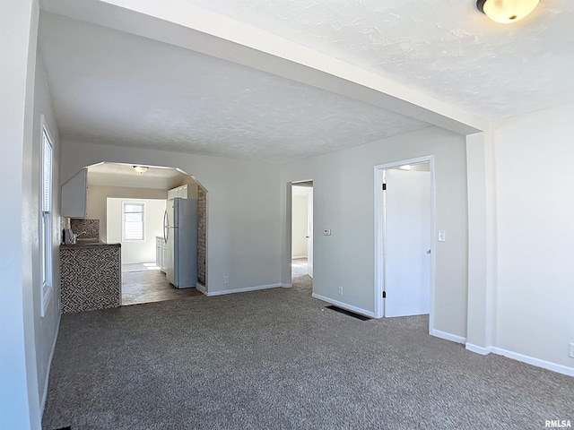 spare room with a textured ceiling, arched walkways, dark colored carpet, and baseboards