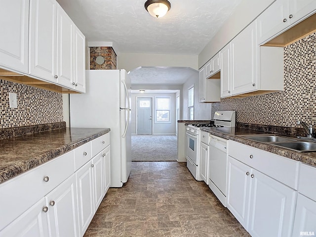 kitchen with white appliances, arched walkways, a sink, white cabinetry, and dark countertops