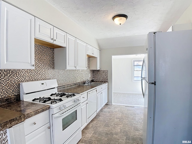 kitchen with a sink, backsplash, dark countertops, white appliances, and white cabinets