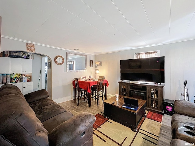 living room featuring arched walkways, ornamental molding, baseboards, and wood finished floors