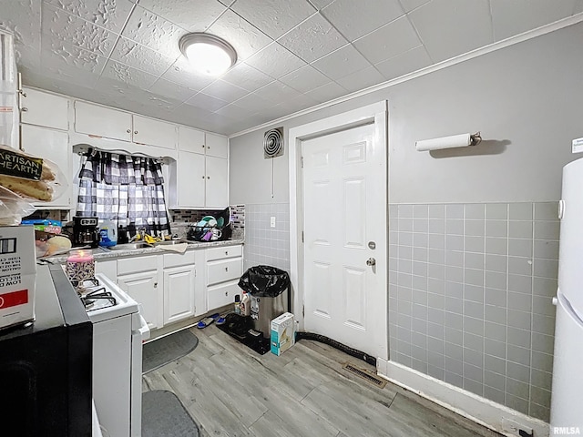 kitchen featuring light wood-style flooring, tile walls, white cabinets, light countertops, and white range with gas stovetop