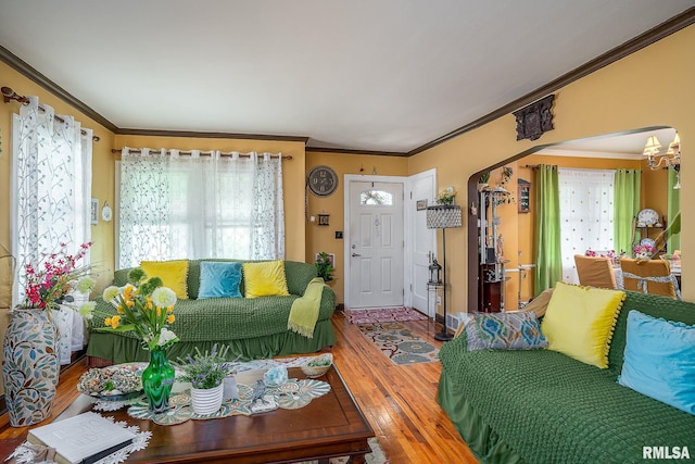 living area featuring ornamental molding, hardwood / wood-style floors, arched walkways, baseboards, and a chandelier