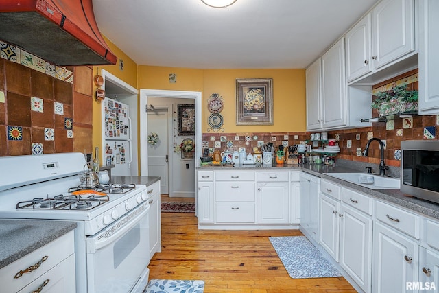 kitchen with under cabinet range hood, light wood-type flooring, white appliances, white cabinetry, and a sink