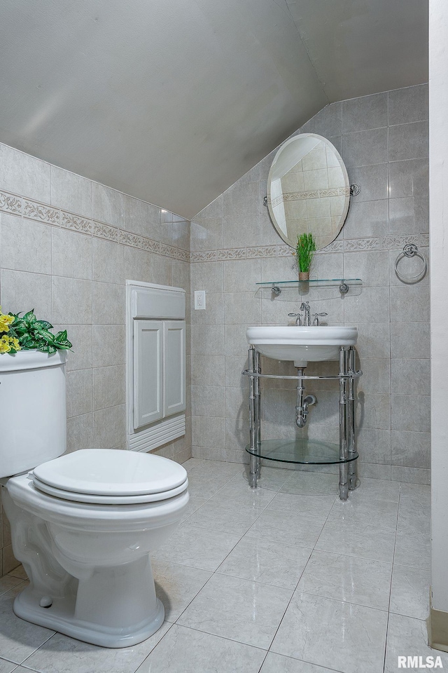 half bathroom with a sink, toilet, tile walls, and vaulted ceiling