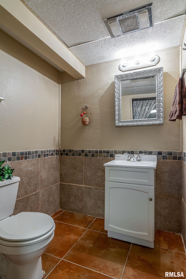 bathroom with visible vents, toilet, tile walls, tile patterned flooring, and vanity