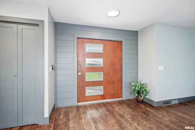 foyer entrance featuring wood walls, visible vents, baseboards, and wood finished floors