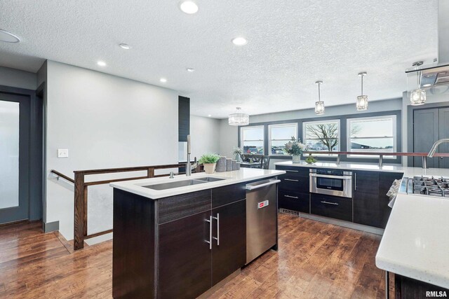 kitchen featuring an island with sink, a textured ceiling, light countertops, appliances with stainless steel finishes, and a sink