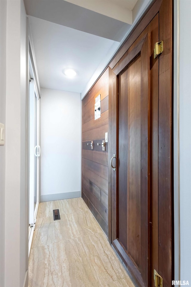 corridor with marble finish floor, wood walls, and baseboards