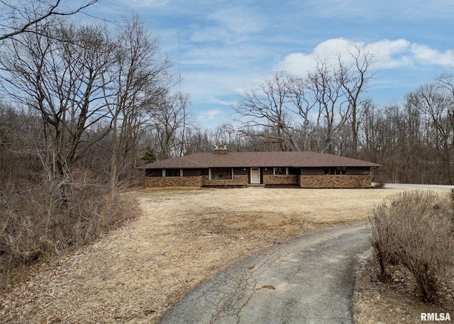 view of front of home featuring stone siding, a chimney, and driveway