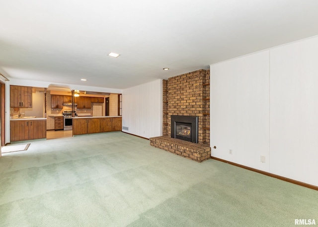 unfurnished living room with light carpet, a brick fireplace, and baseboards