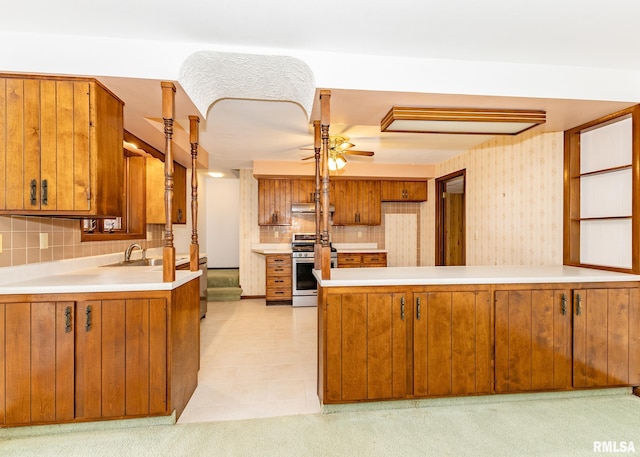 kitchen featuring stainless steel gas range oven, light countertops, brown cabinets, a peninsula, and a ceiling fan