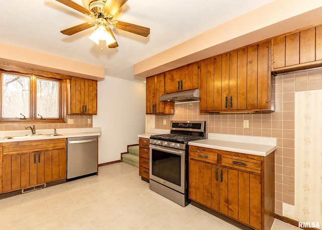 kitchen featuring light countertops, brown cabinets, under cabinet range hood, and stainless steel appliances