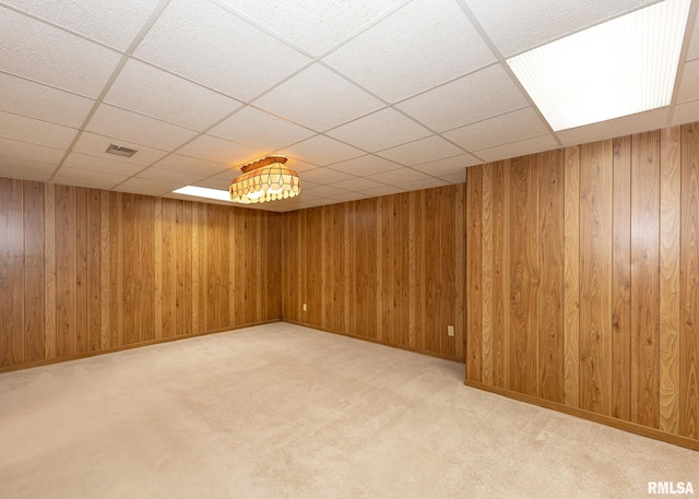 finished below grade area featuring wooden walls, a paneled ceiling, visible vents, and light carpet