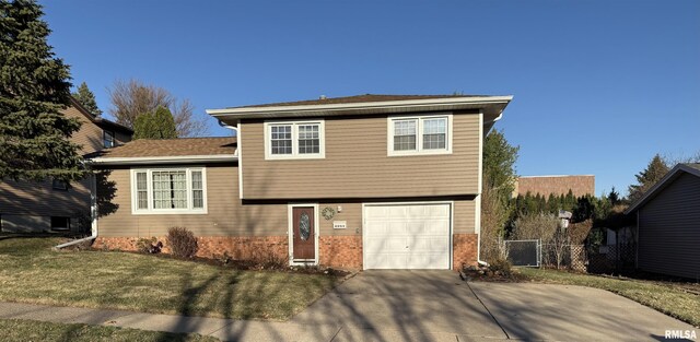 split level home featuring fence, driveway, a front lawn, a garage, and brick siding