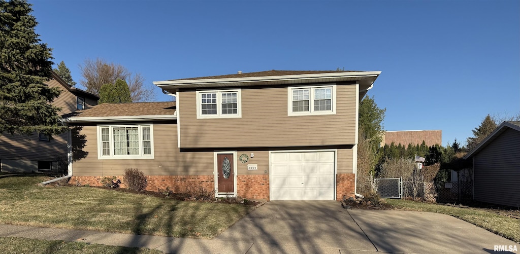 tri-level home featuring fence, a garage, concrete driveway, a front yard, and brick siding