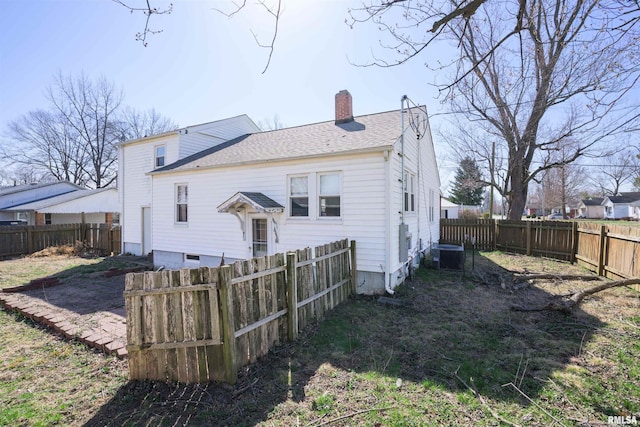 back of house featuring central AC unit, a chimney, a fenced backyard, and a shingled roof