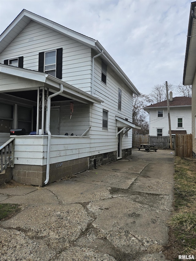 view of side of home featuring covered porch and fence