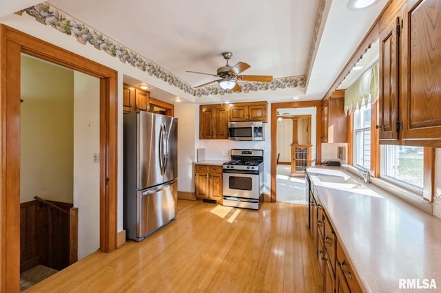 kitchen with brown cabinetry, a sink, light countertops, light wood-style floors, and appliances with stainless steel finishes