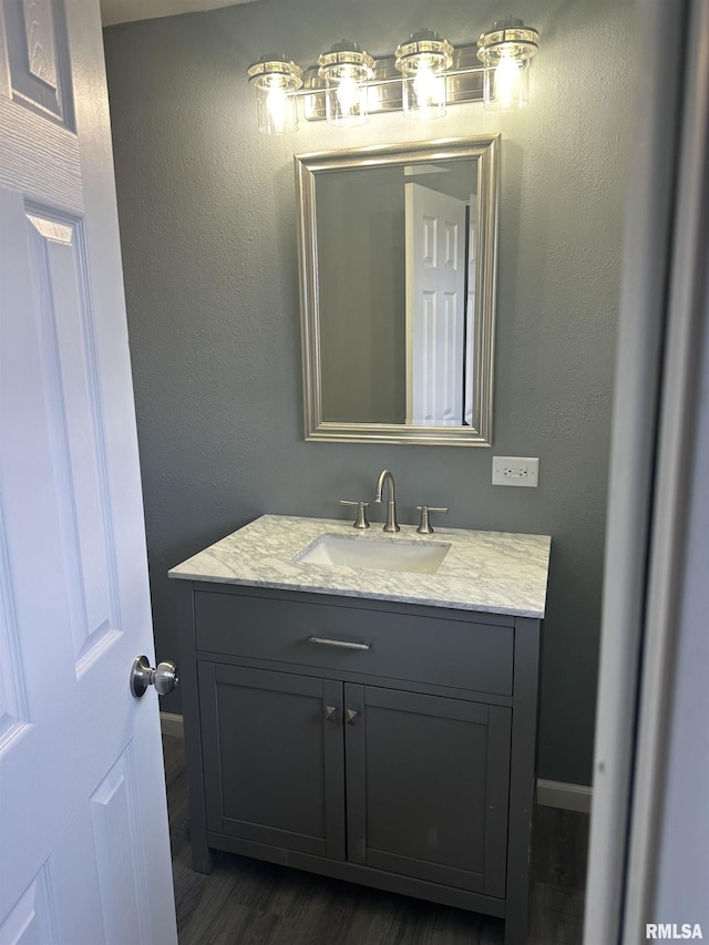 bathroom with vanity, a textured wall, baseboards, and wood finished floors