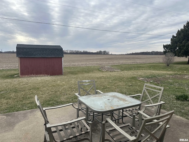 view of patio with a storage unit, outdoor dining space, an outbuilding, and a rural view