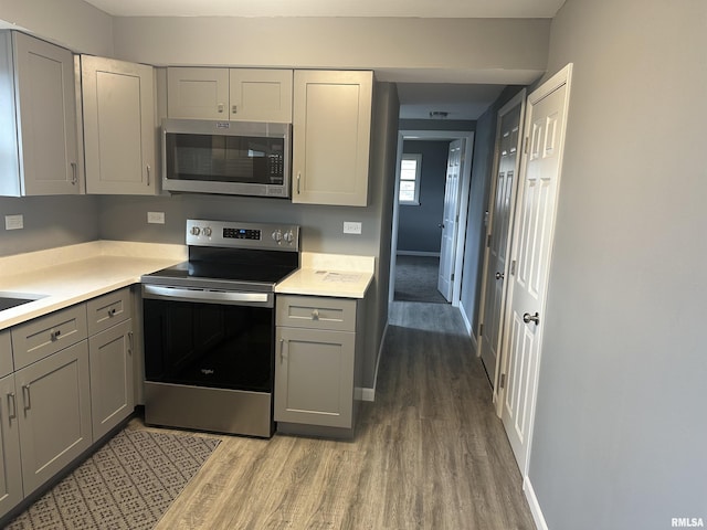 kitchen featuring light countertops, baseboards, gray cabinetry, appliances with stainless steel finishes, and wood finished floors