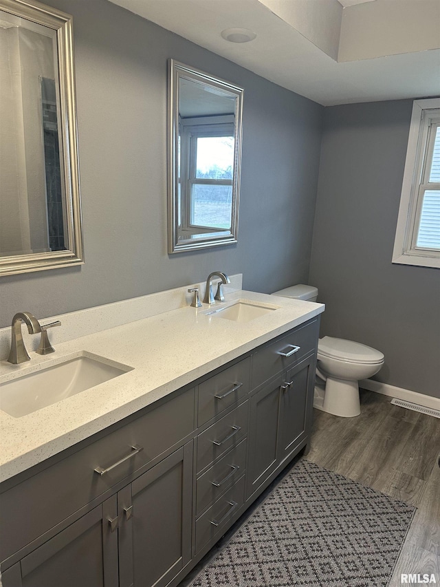 full bathroom with a wealth of natural light, a sink, toilet, and wood finished floors