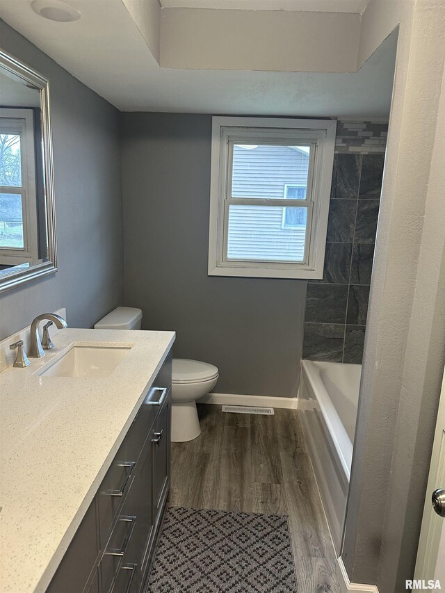 bathroom featuring a bathtub, baseboards, wood finished floors, toilet, and vanity