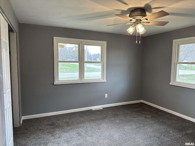 unfurnished room featuring visible vents, baseboards, dark colored carpet, and ceiling fan