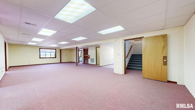 empty room with visible vents, brick wall, carpet floors, a drop ceiling, and stairs