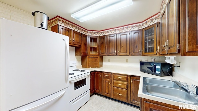 kitchen featuring glass insert cabinets, light countertops, light tile patterned floors, white appliances, and a sink