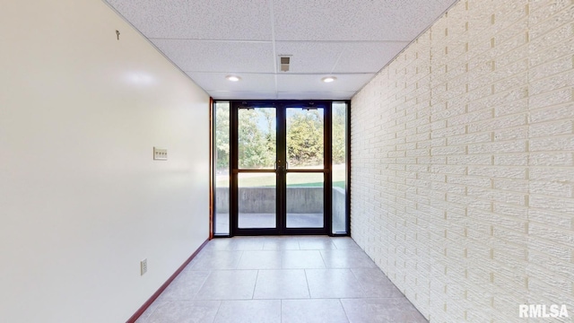 interior space with a drop ceiling, floor to ceiling windows, french doors, light tile patterned floors, and baseboards
