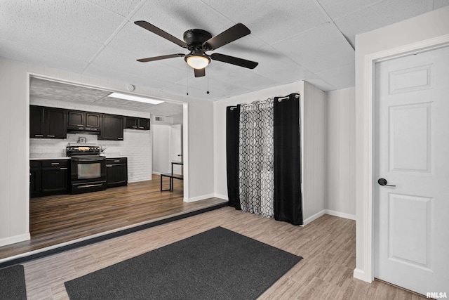 interior space with a drop ceiling, baseboards, wood finished floors, and a ceiling fan