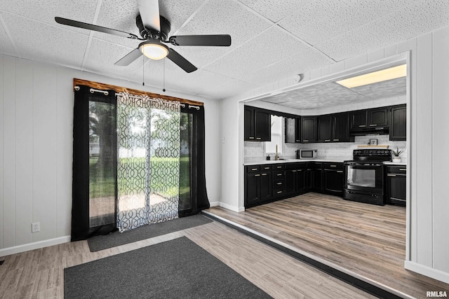 kitchen with dark cabinetry, black / electric stove, a sink, light wood-style floors, and under cabinet range hood