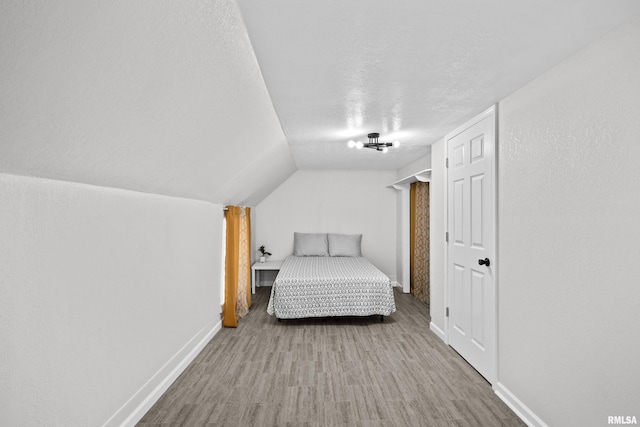 bedroom featuring vaulted ceiling, a textured ceiling, baseboards, and wood finished floors