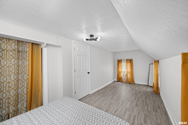bedroom featuring baseboards, a textured ceiling, lofted ceiling, and wood finished floors