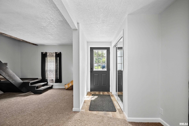 entrance foyer featuring baseboards, light carpet, and a textured ceiling