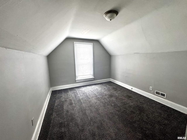 additional living space featuring visible vents, dark carpet, lofted ceiling, and baseboards